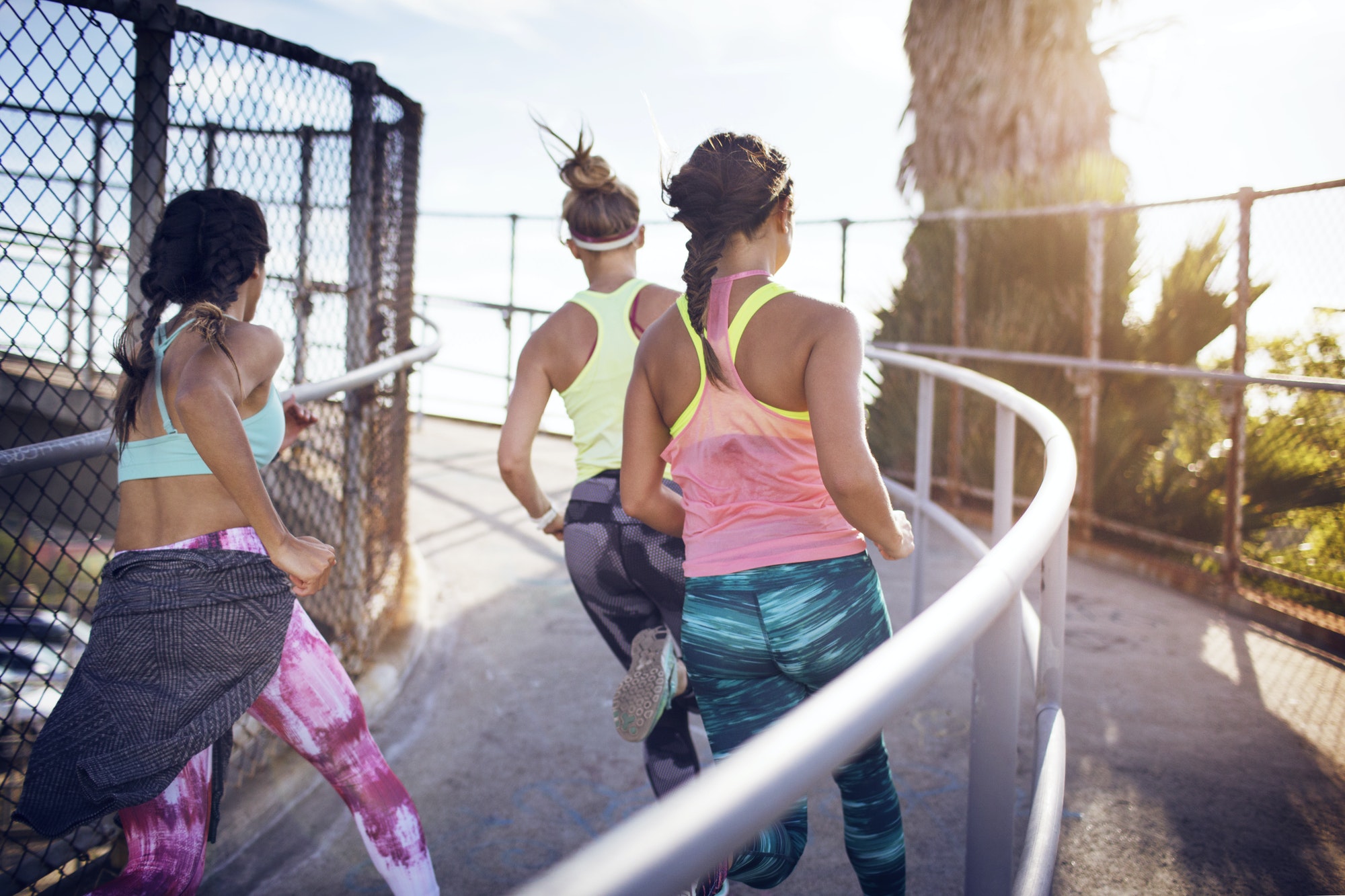 Rear View Of Athletes Jogging On Bridge Against Sky